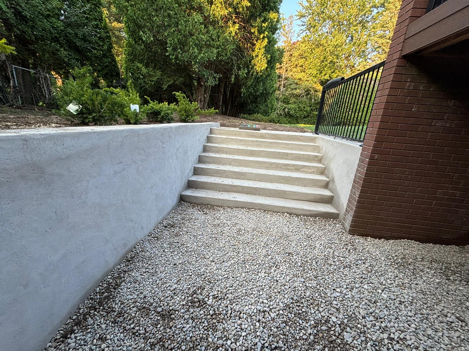 Finished parged poured concrete retaining wall flanking a concrete staircase beside a brick home